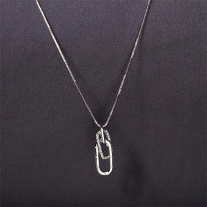 A gold-plated sterling silver letter interlocking pin pendant necklace with cubic zirconia, displayed on a yellow background.