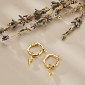 Gold hoop earrings with lightning bolt charms on a beige background with dried lavender.