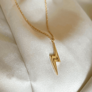 Gold lightning bolt necklace on a soft beige fabric background