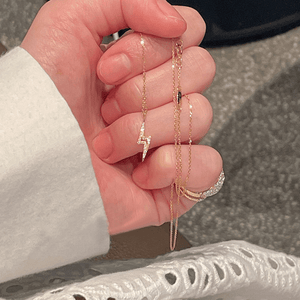 Hand wearing multiple gold necklaces and rings on a neutral background