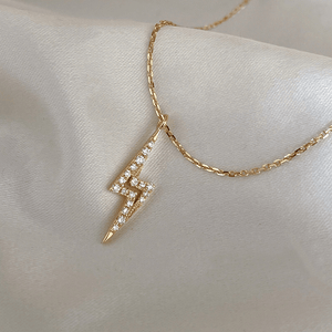 A gold-plated sterling silver lightning bolt pendant necklace with cubic zirconia, displayed against a white fabric background.