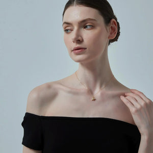 Woman wearing a black off-shoulder top and a delicate necklace against a plain background