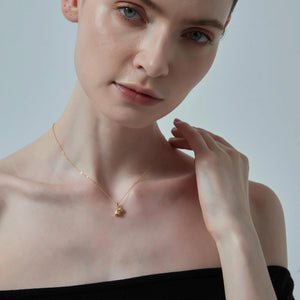 Woman wearing a gold necklace with a small pendant against a plain background