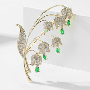 Gold leaf-shaped brooch with green gemstones on a white background