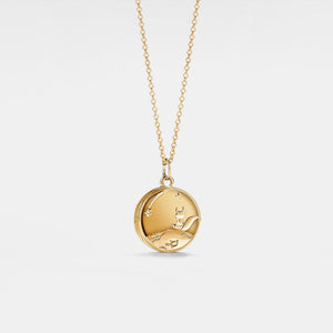 Gold necklace with a round locket featuring a fox and stars on a light gray background, inspired by 'The Little Prince'.