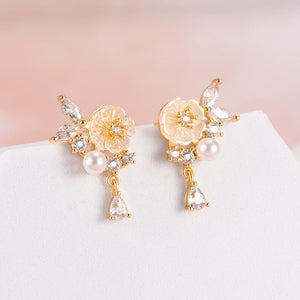 Pair of gold earrings with floral and pearl designs on a white surface.