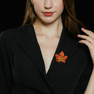 Woman wearing a black blazer with a red maple leaf brooch against a dark background