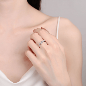 Close-up of a hand wearing a silver ring with a clear gemstone against a neutral background