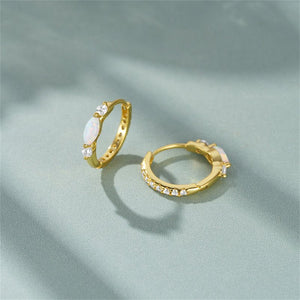 Gold hoop earrings with embedded stones on a light green fabric background