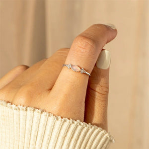 Two gold-plated sterling silver rings with opal centers and cubic zirconia on either side, displayed on a textured surface.