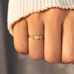 Two gold-plated sterling silver rings with opal centers and cubic zirconia on either side, displayed on a textured surface.