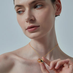 Woman wearing a gold necklace with a pendant against a neutral background