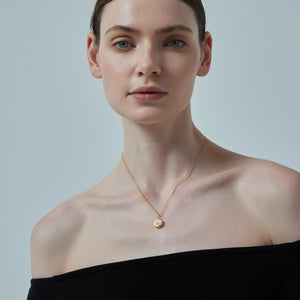 Woman wearing a gold necklace with a pendant against a plain background