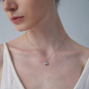 Close-up of a woman wearing a delicate necklace with a small star locket pendant on a plain background