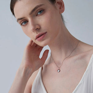 Woman wearing a delicate necklace with a star locket pendant against a plain background
