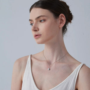 Woman wearing a delicate necklace with a star locket pendant against a plain background