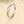 A silver wedding ring with a central cubic zirconia surrounded by smaller clear crystals, held by a shadow on a beige background.