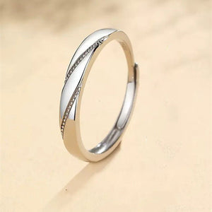 A silver wedding ring with a central cubic zirconia surrounded by smaller clear crystals, held by a shadow on a beige background.