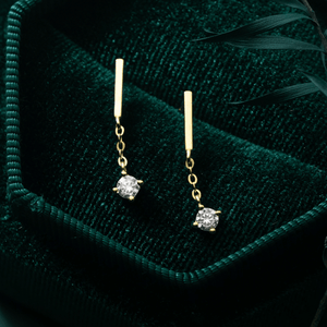 Gold earrings with diamond drops on a green velvet surface