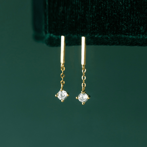 Gold earrings with clear gemstones on a green background