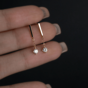 Gold earrings with small gemstones held between fingers against a dark background