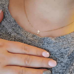 Gold necklace with a cross pendant worn by a person on a textured fabric background