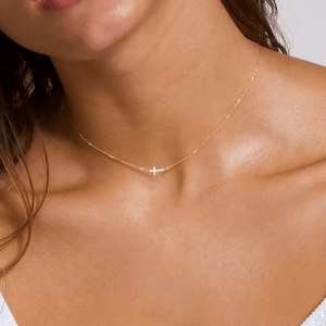 Close-up of a person wearing a gold necklace with a cross pendant.