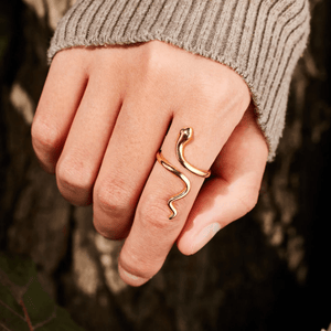 Gold snake-shaped ring on a person's finger with a blurred natural background