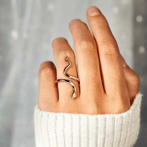Hand wearing a gold ring with a snake design against a neutral background