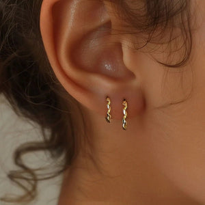 Close-up of an ear wearing gold hoop earrings with a neutral background