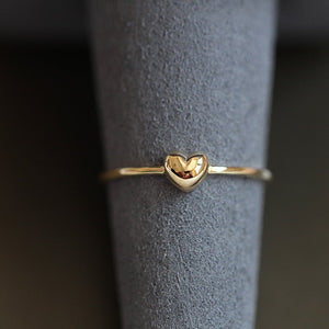 Gold heart-shaped ring on a gray cylindrical stand with a blurred background