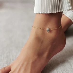 Gold anklet with a crystal on a foot against a neutral background
