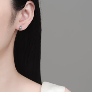 Close-up of a person wearing a silver earring with a clear gemstone on a gray background