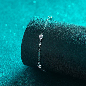 Silver bracelet with small round charms on a textured teal surface