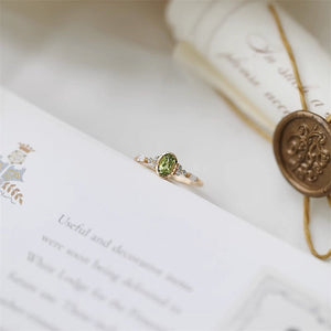 Gold ring with a green gemstone on an open book with a wax seal.