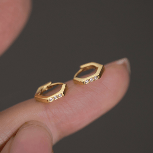 Gold hoop earrings with small diamonds on a finger against a dark background