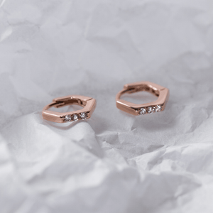 Rose gold hoop earrings with small diamonds on a white fabric background