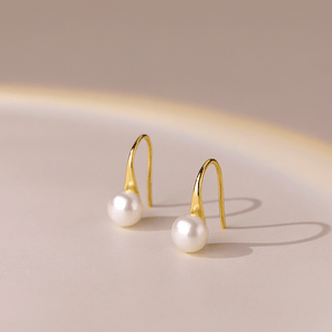 Gold earrings with pearl drops on a beige background