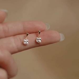 Gold earrings with small crystals held between fingers against a beige background
