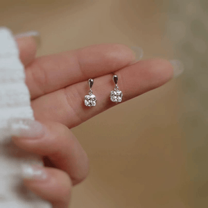 Silver earrings held between fingers against a blurred background