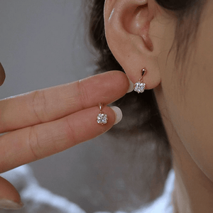 Gold earrings with clear gemstones worn by a person, held up to the ear.