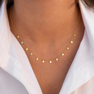 Gold necklace with small round pendants on a person wearing a white shirt.
