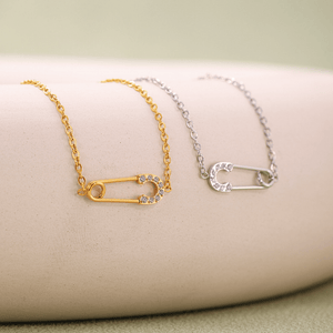 Gold and silver necklaces with safety pin designs on a beige surface.