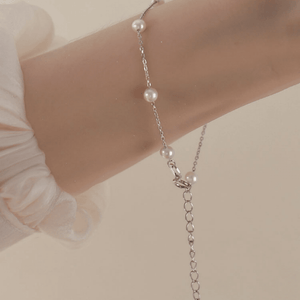 Pearl necklace on a person's wrist against a neutral background