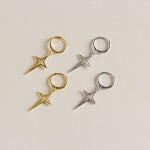 Two pairs of star-shaped earrings, one gold and one silver, on a light beige background.