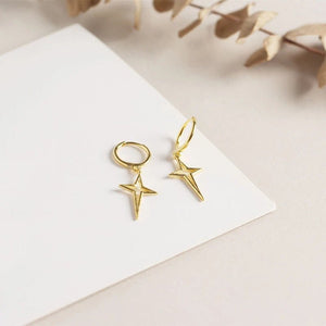 Gold star-shaped earrings on a white card with a beige background
