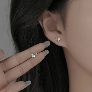 Close-up of an ear wearing a silver earring with a hand holding another similar earring.
