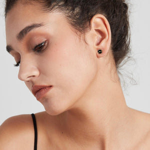 Close-up of a woman wearing black earrings on a light background