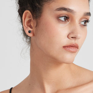 Close-up of a woman wearing a black earring on a plain background