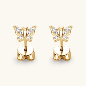 Gold butterfly earrings with clear gemstones on a light beige background